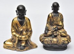 Budas, conjunto de duas estatuetas chinesas a gosto da dinastia Ching, em material sintético ebanizado e realçado a ouro brunido, med. 15 x 24cm e 17 x 23cm.