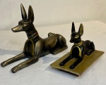 Dupla de cães egípcios em resina com ornamentação em dourados. Medidas: Maior 15cm comp e o Menor 9cm comp.