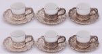 Seis xícaras para café em porcelana branca, marca Mauá. Suportes e pires em prata marcados, M.K. 800. Borda decorada com volutas formando bicos, folhas e pingentes em alto relevo. Peso 565,3 g.