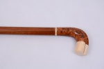 Robusta bengala em madeira de radica, apoio sugerindo mão em radica, detalhe com filete em marfim e robusto acabamento de topo também em marfim. Ponteira de osso. Altura 92 cm.
