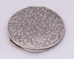 Poseira redonda em prata 800 contrastada, superfície decorada com arabescos, espelho interno e almofada original. Diâmetro 8,5 cm. Peso 72,6 g.