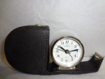 Antigo relógio de viagem, acoplado em estojo de couro original, movimento quartz, mostrador em porcelana, caixa em aço, medida do estojo=7 x 6.5 cm, diâmetro do relógio=5 x 4.7 cm.