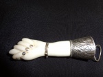 Grande figa em porcelana, acabamento em prata, 7 x 2 cm. A unha do dedo mínimo está faltando a prata.