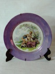 Prato de coleção em porcelana com borda na cor lilás com galeria central decorada com Cena galante. Med.: 25 cm.