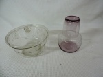 Lote constando duas peças em vidro lavrado sendo: um verre deau na cor lilás e um baleiro com tampa lavrado com cachos de uvas.