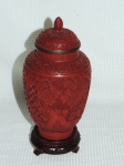 Potiche confeccionado em laca chinesa na cor vermelha ricamente entalhado com flores e acanto e pega da tapa na forma de pinha. acompanha base em madeira. Med.: 21 cm.