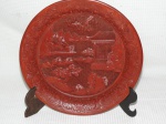 Medalhão confeccionado em laca chinesa na cor vermelha ricamente entalhado com Cena de pagode e arvores na galeria central em relevo.Med.: 26 cm.