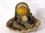 Pequena fonte em resina policromada decorada com flores e sol na parte superior e base na forma de concha. Med.: 25cm x 27cm